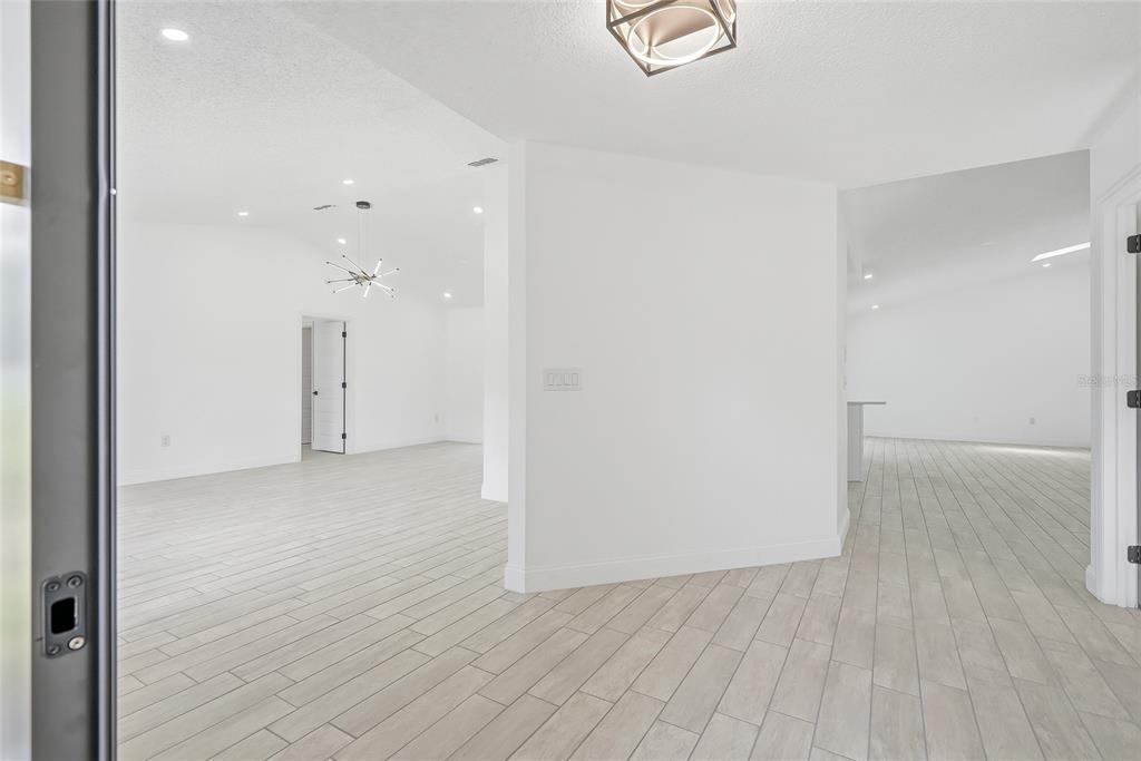 A bright, open-concept living area features white walls, light wood-look tile flooring, and modern decor — 2462 STEPHANIE DRIVE, SPRING HILL, FL