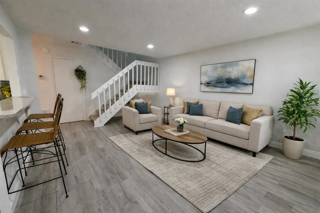 A living room features light wood-look flooring, a staircase, a sofa, an armchair, and stools — 4402 RING NECK ROAD UNIT 19B, ORLANDO, FL