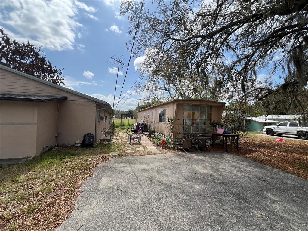 A paved driveway leads to a mobile home situated next to a tan house — 617 E MYERS BOULEVARD, MASCOTTE, FL