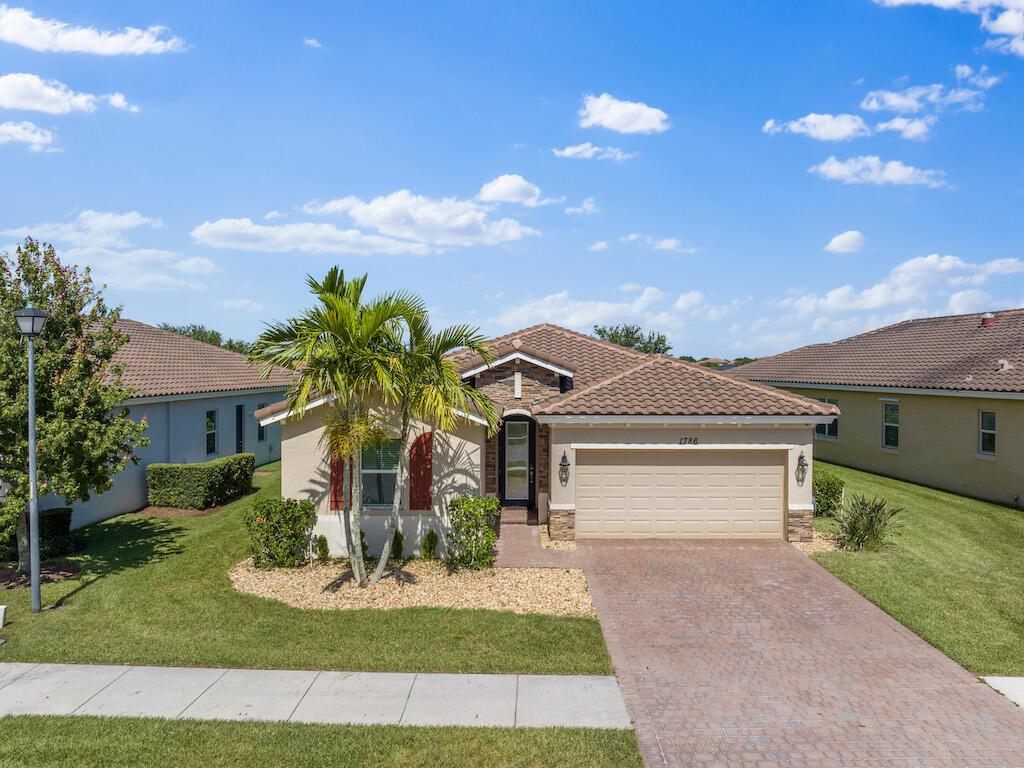 A single-story suburban house with a tan stucco exterior, tile roof, and brick paver driveway — 1786 Berkshire Circle SW, Vero Beach FL 32968, VERO BEACH, FL