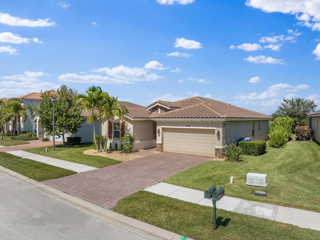 A single-story suburban house with a tan stucco exterior, tile roof, and brick paver driveway — 1786 Berkshire Circle SW, Vero Beach FL 32968, VERO BEACH, FL