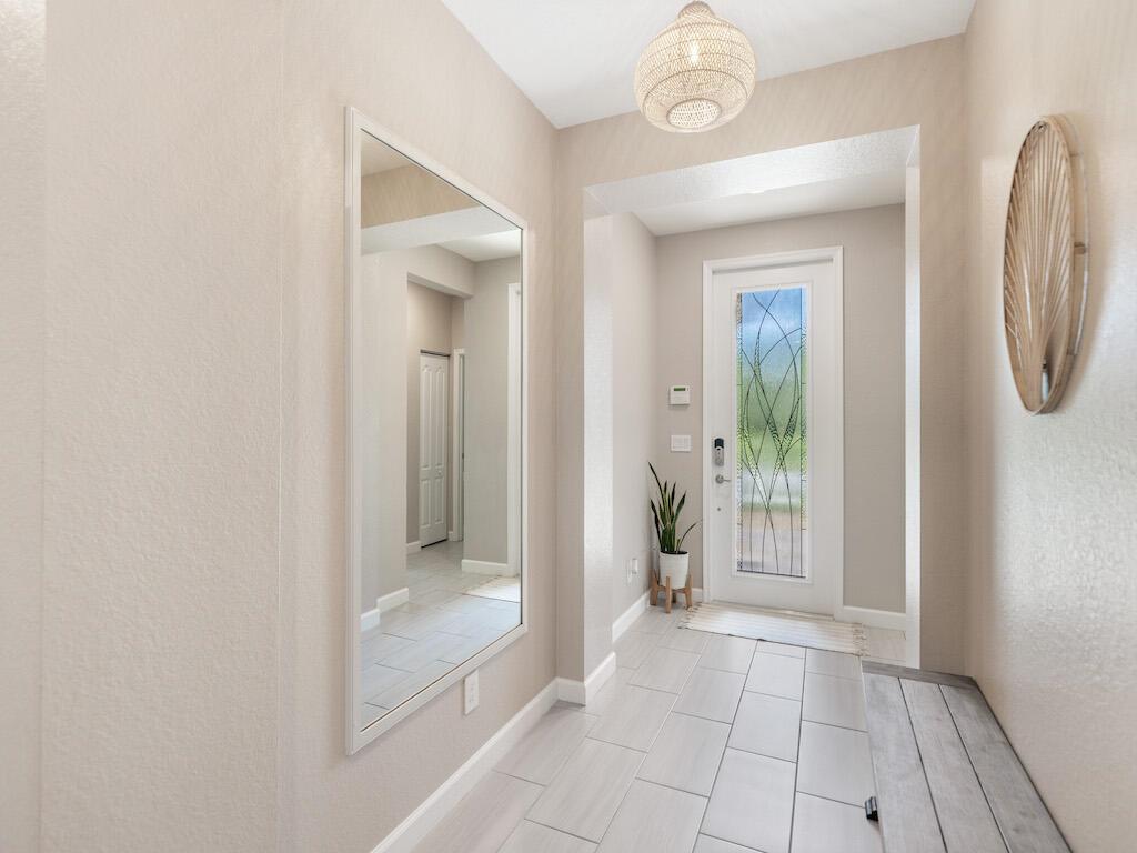 A bright entryway features a large wall mirror, a wooden bench, and a glass-paneled door — 1786 Berkshire Circle SW, Vero Beach FL 32968, VERO BEACH, FL