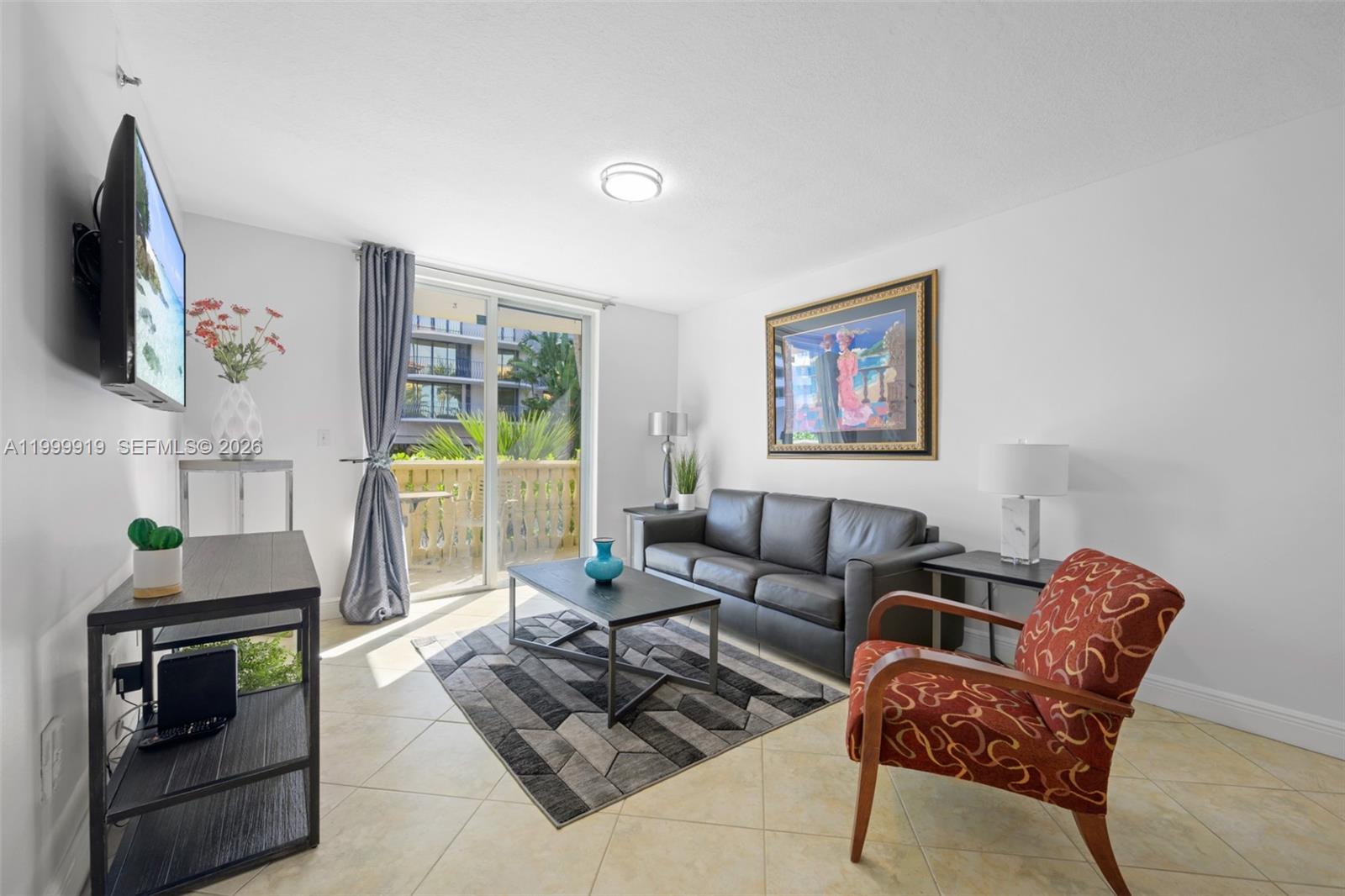 A living room features a black leather sofa, patterned armchair, coffee table, and balcony access — 8888 Collins Ave # 105, Surfside FL 33154, SURFSIDE, FL