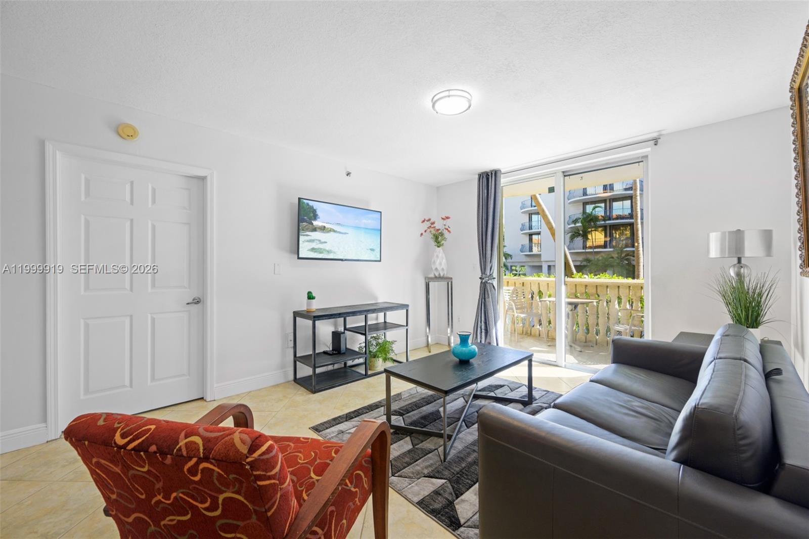A living room features a black leather sofa, patterned armchair, and a balcony with seating — 8888 Collins Ave # 105, Surfside FL 33154, SURFSIDE, FL