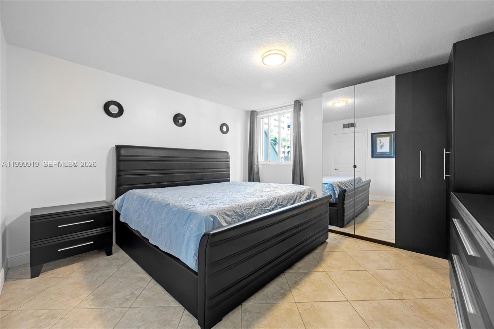 A bedroom features a black bed frame, matching furniture, mirrored closet doors, and tile flooring — 8888 Collins Ave # 105, Surfside FL 33154, SURFSIDE, FL