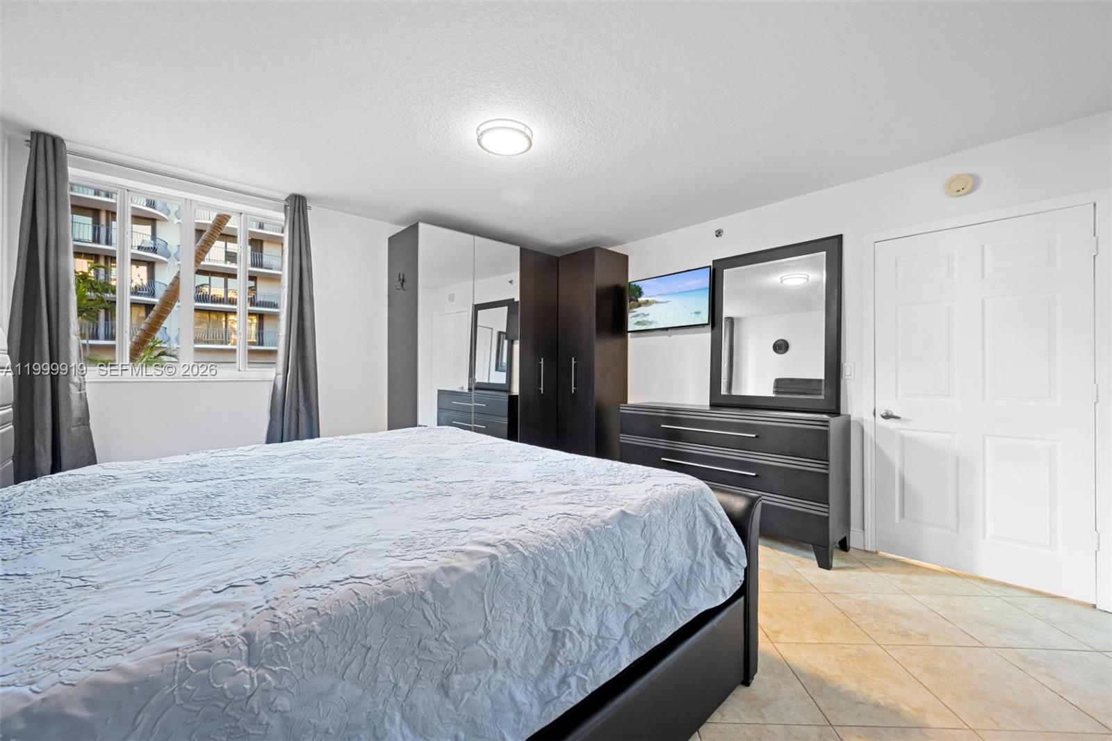A bedroom features a bed, dark wood furniture, a wall-mounted television, and tile flooring — 8888 Collins Ave # 105, Surfside FL 33154, SURFSIDE, FL