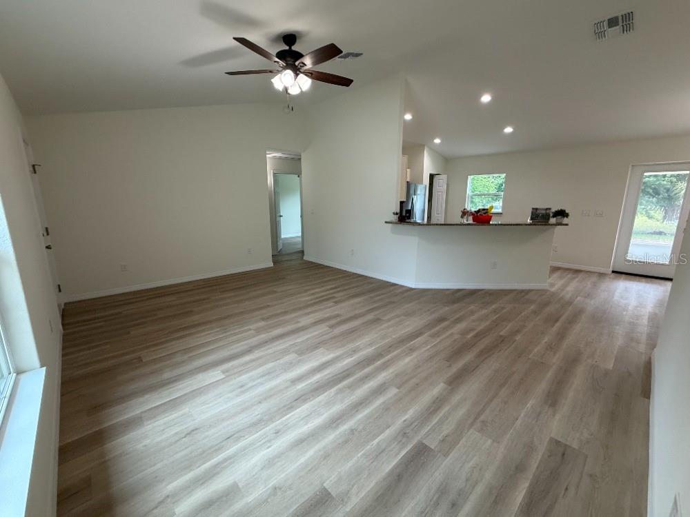 An open-concept living area features light wood-look flooring, a ceiling fan, and a kitchen peninsula — 20115 SW 83RD PLACE, DUNNELLON, FL