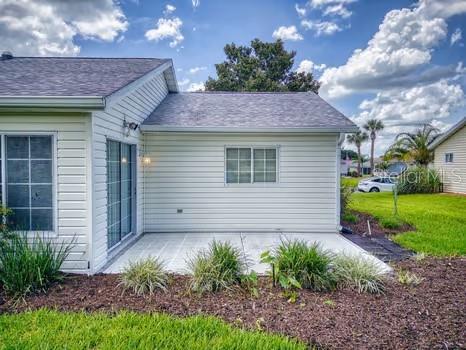 The exterior of a house features light-colored siding, a concrete patio, and a grassy yard — 13729 SE 89TH AVENUE, SUMMERFIELD, FL
