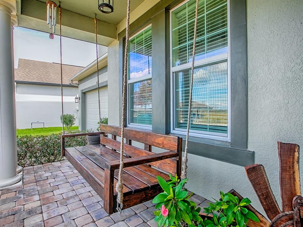 A wooden porch swing hangs on a paved patio in front of a house — 417 BLUE CYPRESS DRIVE, GROVELAND, FL