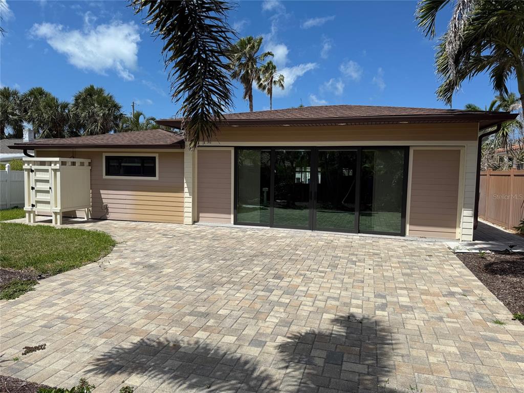 A paved patio sits in front of a house with tan siding and large sliding doors — 833 LANTANA AVENUE, CLEARWATER BEACH, FL
