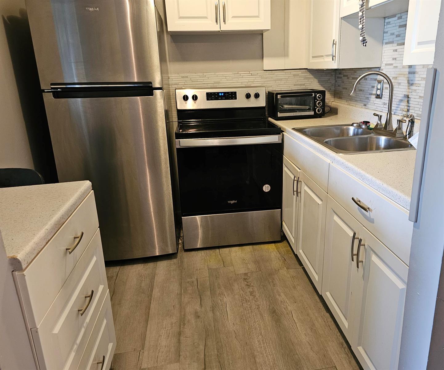A kitchen features stainless steel appliances, white cabinets, light countertops, and wood-look flooring — 102 Easthampton E, West Palm Beach FL 33417, WEST PALM BEACH, FL