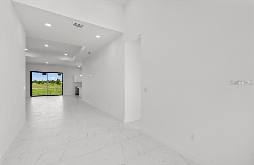 A bright, open-concept room features white walls, white marble-look tile flooring, and a sliding glass door — 3927 NW 40TH TERRACE, CAPE CORAL, FL