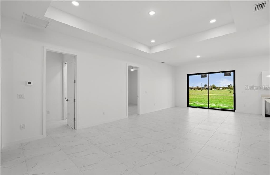 A bright, white-tiled room features a tray ceiling, recessed lighting, and sliding glass doors — 3927 NW 40TH TERRACE, CAPE CORAL, FL