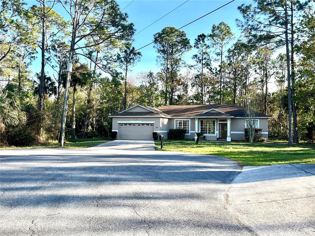 A single-story house with a two-car garage sits on a lot surrounded by tall trees — 14 SQUASH BLOSSOM COURT, PALM COAST, FL