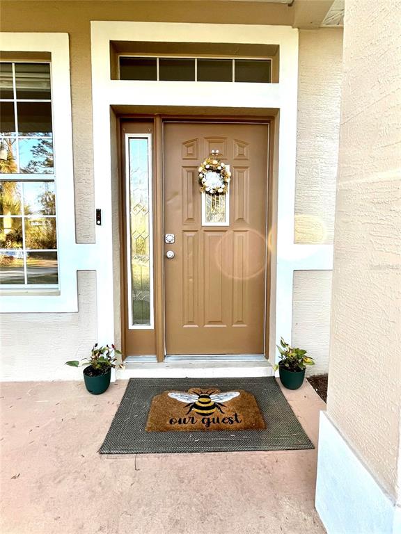 A brown front door with a decorative wreath sits between a window and a sidelight — 14 SQUASH BLOSSOM COURT, PALM COAST, FL