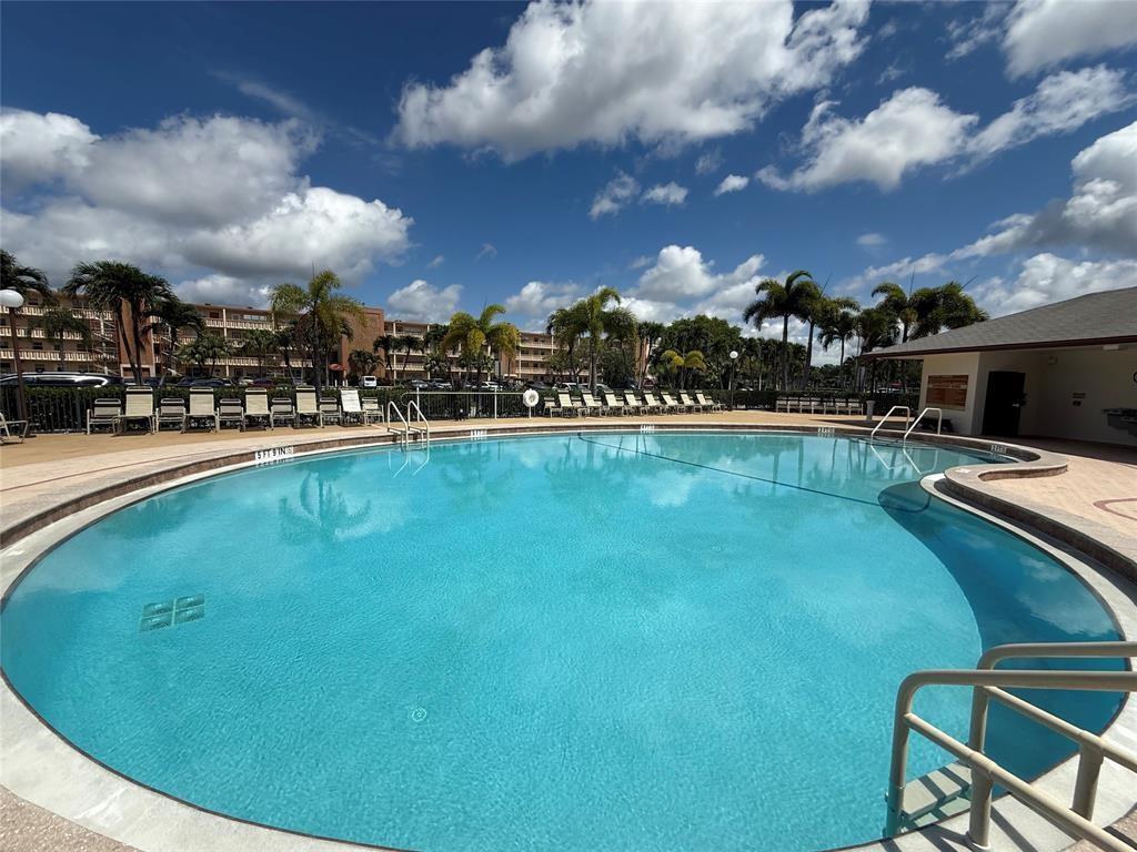 A large outdoor swimming pool is surrounded by lounge chairs, palm trees, and apartment buildings — 84 Mansfield B # 84, Boca Raton FL 33434, BOCA RATON, FL