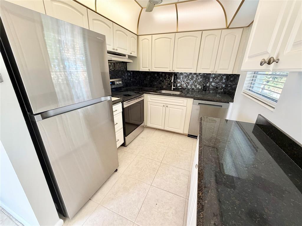 A kitchen features white cabinets, stainless steel appliances, black granite countertops, and a tiled backsplash — 84 Mansfield B # 84, Boca Raton FL 33434, BOCA RATON, FL