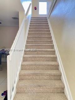 A carpeted staircase with white railings leads upward toward a landing with a window — 1906 SE 18th St, Homestead FL 33035, HOMESTEAD, FL