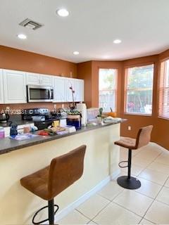 A kitchen features white cabinets, a microwave, a breakfast bar with two stools, and tile flooring — 1906 SE 18th St, Homestead FL 33035, HOMESTEAD, FL