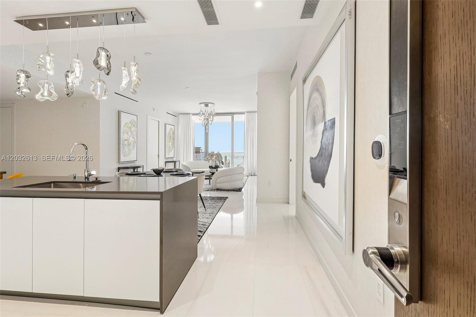 A modern kitchen island with a sink overlooks an open-concept living area with white floors — 300 Biscayne Boulevard Way # 3305W, Miami FL 33131, MIAMI, FL