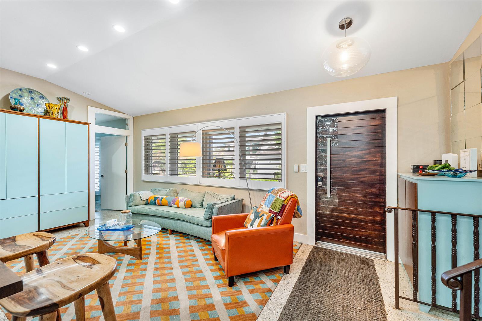 A living room features a mid-century modern aesthetic, a colorful rug, and a wood-paneled door — 1455 NE 4th Avenue, Boca Raton FL 33432, BOCA RATON, FL