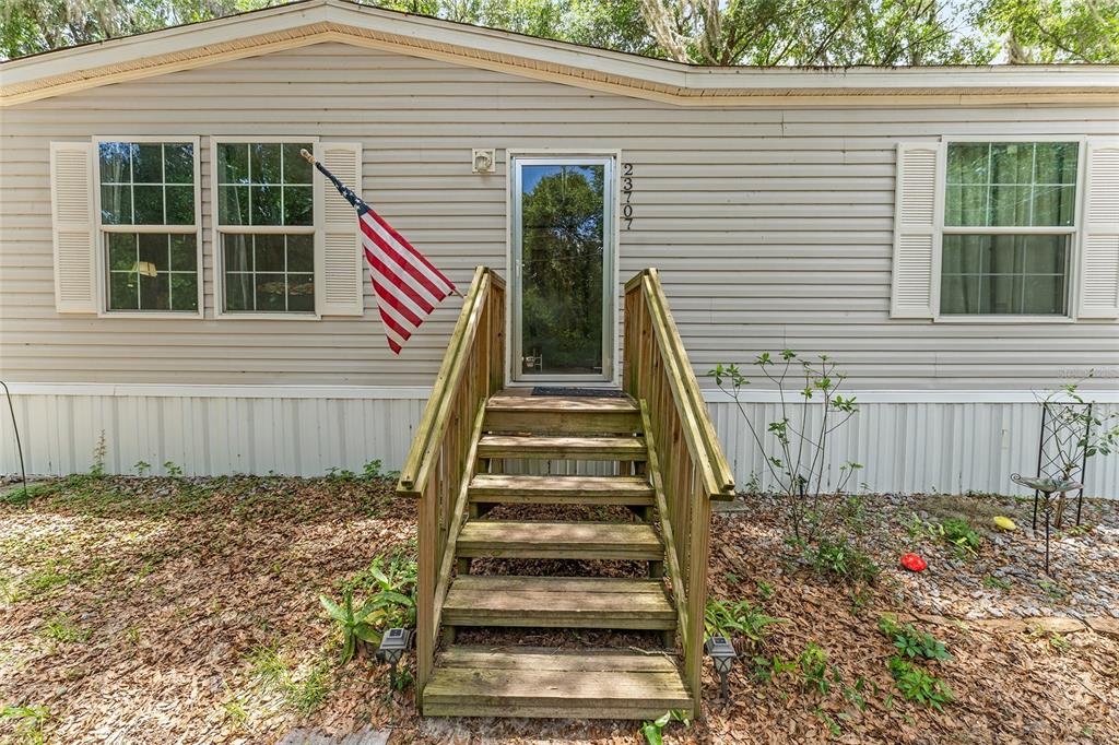 The exterior of a manufactured home features light siding, a wooden staircase, and an American flag — 23707 NE STATE ROAD 26, MELROSE, FL