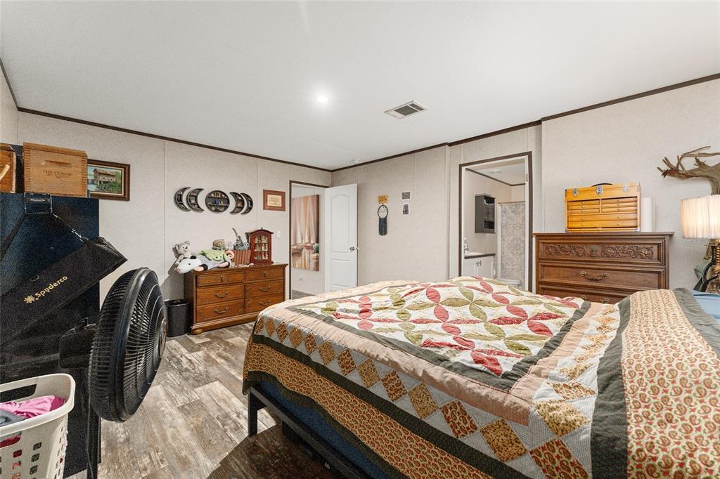 A bedroom with wood-look flooring, a bed, a black wardrobe, and a wooden dresser — 23707 NE STATE ROAD 26, MELROSE, FL