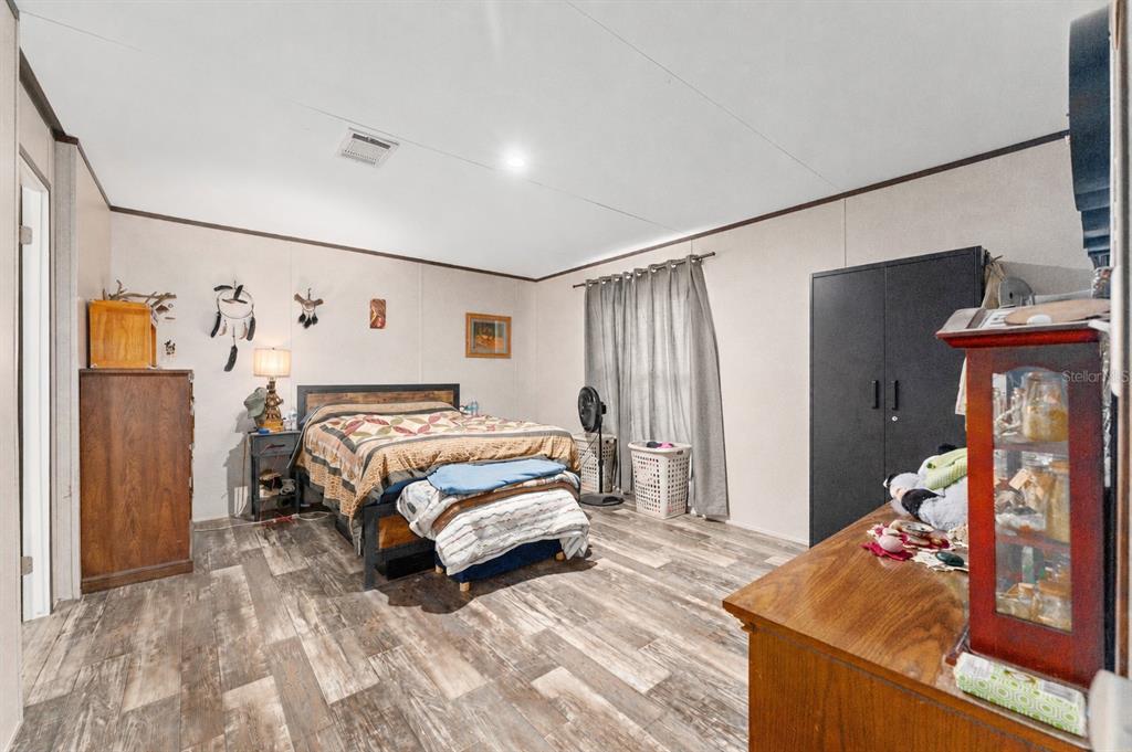A bedroom with a quilt-covered bed, wood-look flooring, a black wardrobe, and a wooden dresser — 23707 NE STATE ROAD 26, MELROSE, FL