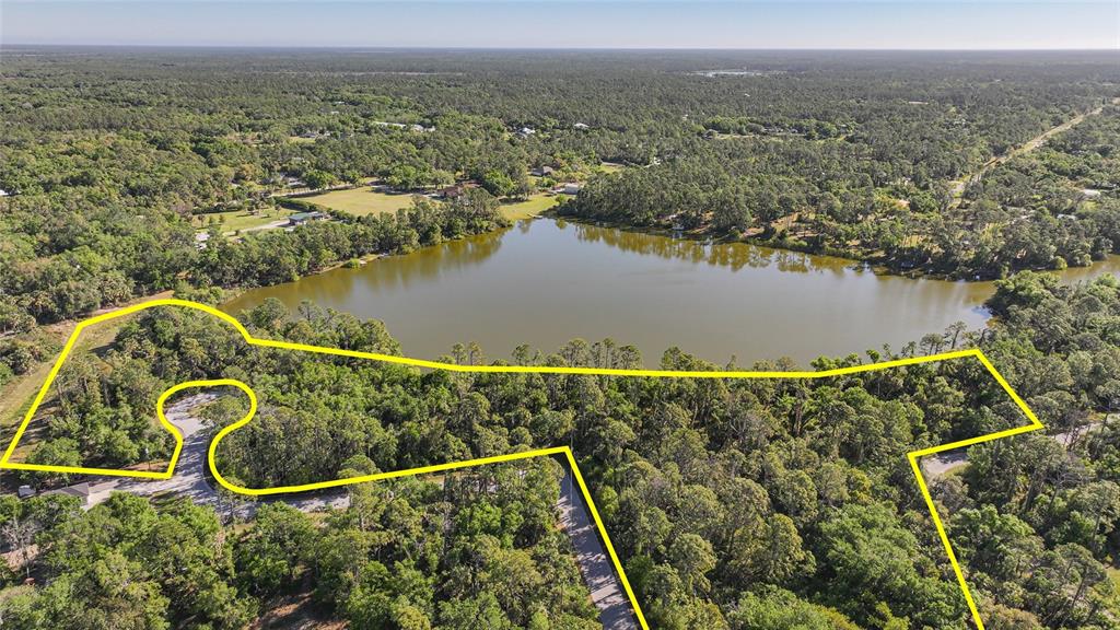 An aerial view shows a wooded lot outlined in yellow bordering a large lake — LONGWELL LANE, NORTH PORT, FL