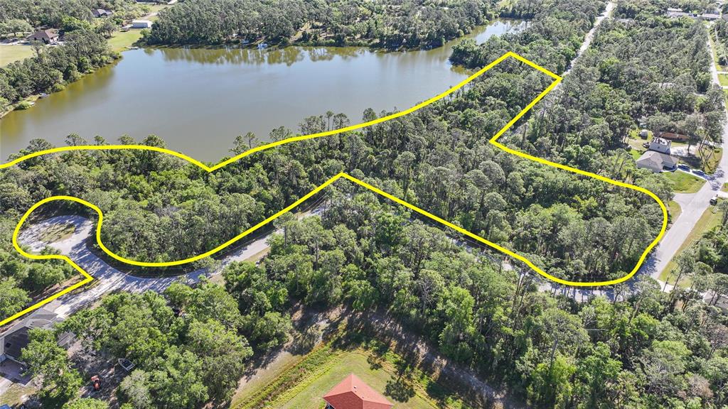 An aerial view shows a wooded lot outlined in yellow next to a lake — LONGWELL LANE, NORTH PORT, FL
