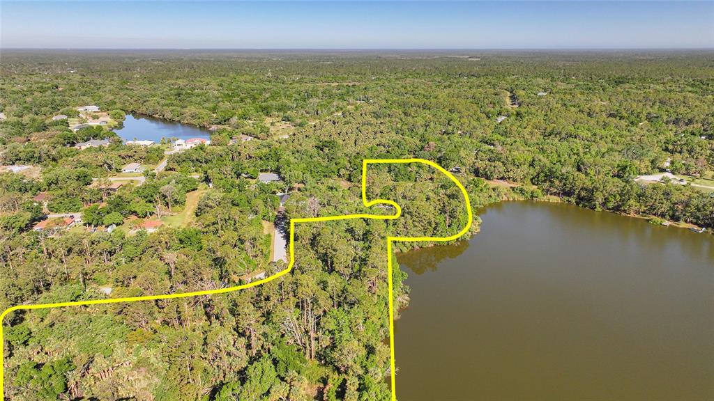 An aerial view shows a wooded lot outlined in yellow bordering a large lake — LONGWELL LANE, NORTH PORT, FL