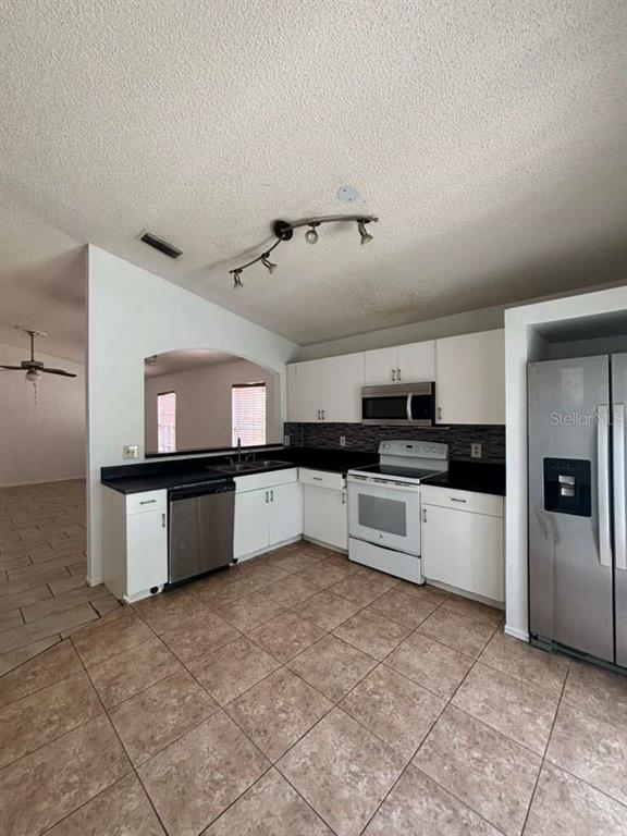 A kitchen features white cabinets, black countertops, stainless steel appliances, and tan tile flooring — 2713 PALM ISLE WAY, ORLANDO, FL