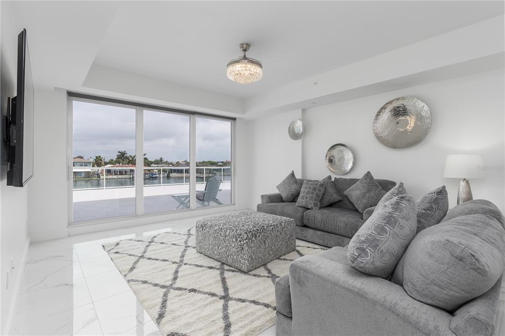 A living room features gray sofas, a patterned ottoman, a white rug, and floor-to-ceiling windows — 415 ISLAND WAY UNIT 207, CLEARWATER BEACH, FL