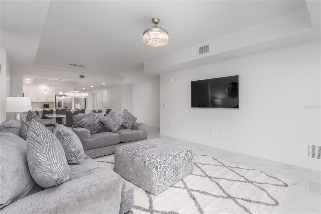 A living room features a grey sofa, a matching ottoman, and a wall-mounted television — 415 ISLAND WAY UNIT 207, CLEARWATER BEACH, FL