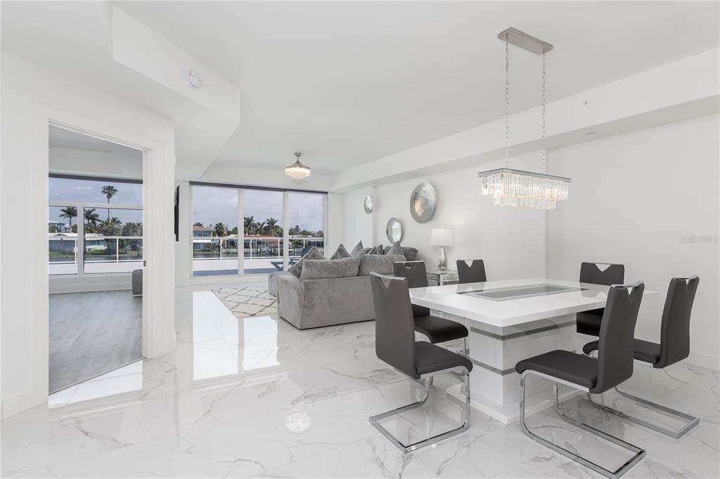 A modern dining and living area features white marble floors, a crystal chandelier, and balcony views — 415 ISLAND WAY UNIT 207, CLEARWATER BEACH, FL