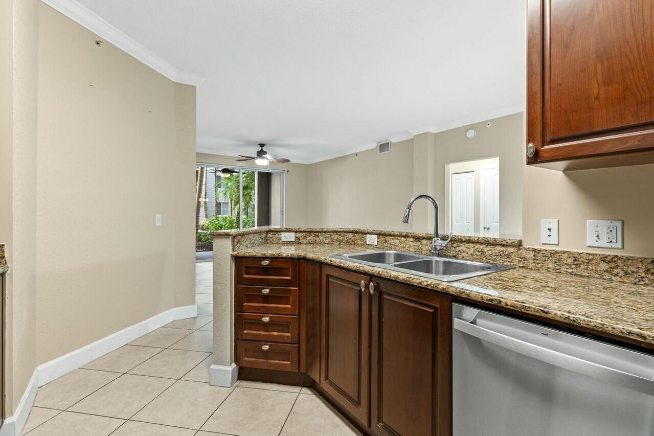 A kitchen features dark wood cabinets, granite countertops, a stainless steel sink, and tile flooring — 1690 Renaissance Commons Boulevard # 1125, Boynton Beach FL 33426, BOYNTON BEACH, FL