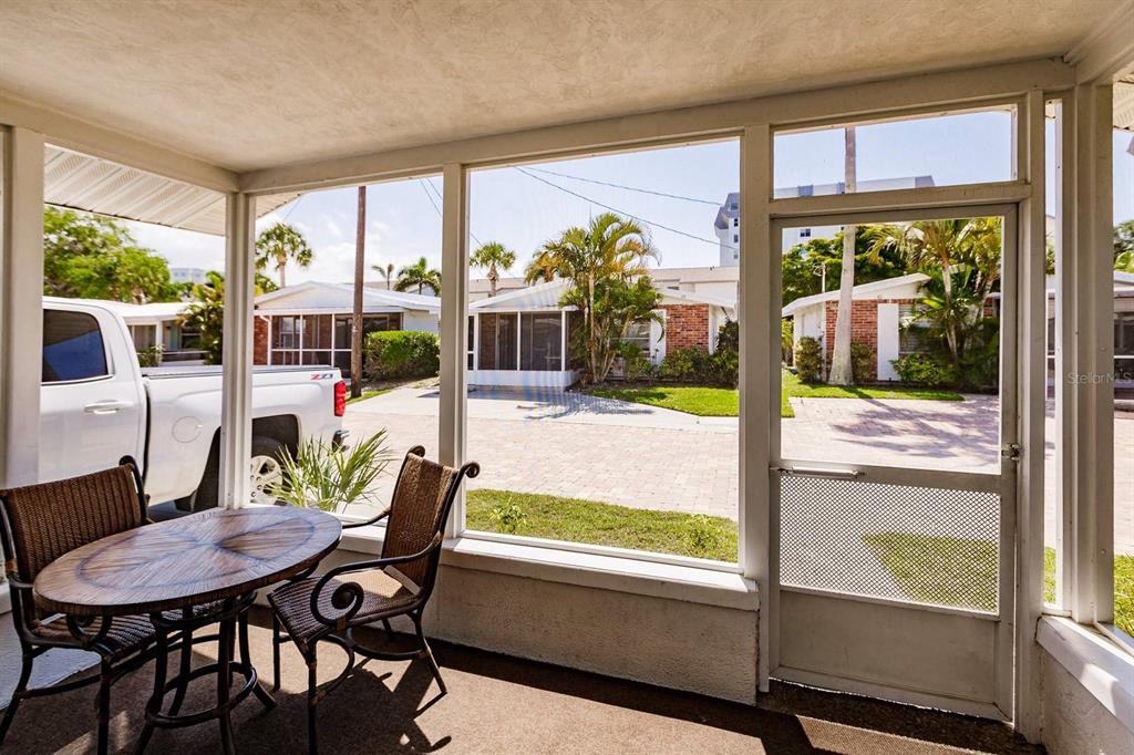 A screened-in porch features a small round table with two chairs overlooking a paved driveway — 6020 MIDNIGHT PASS ROAD UNIT 61, SARASOTA, FL