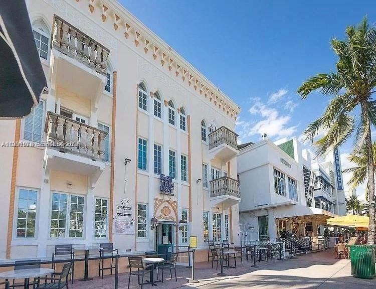 A multi-story building with balconies and arched windows stands along a sunny outdoor pedestrian walkway — 918 Ocean Dr # 302, Miami Beach FL 33139, MIAMI BEACH, FL