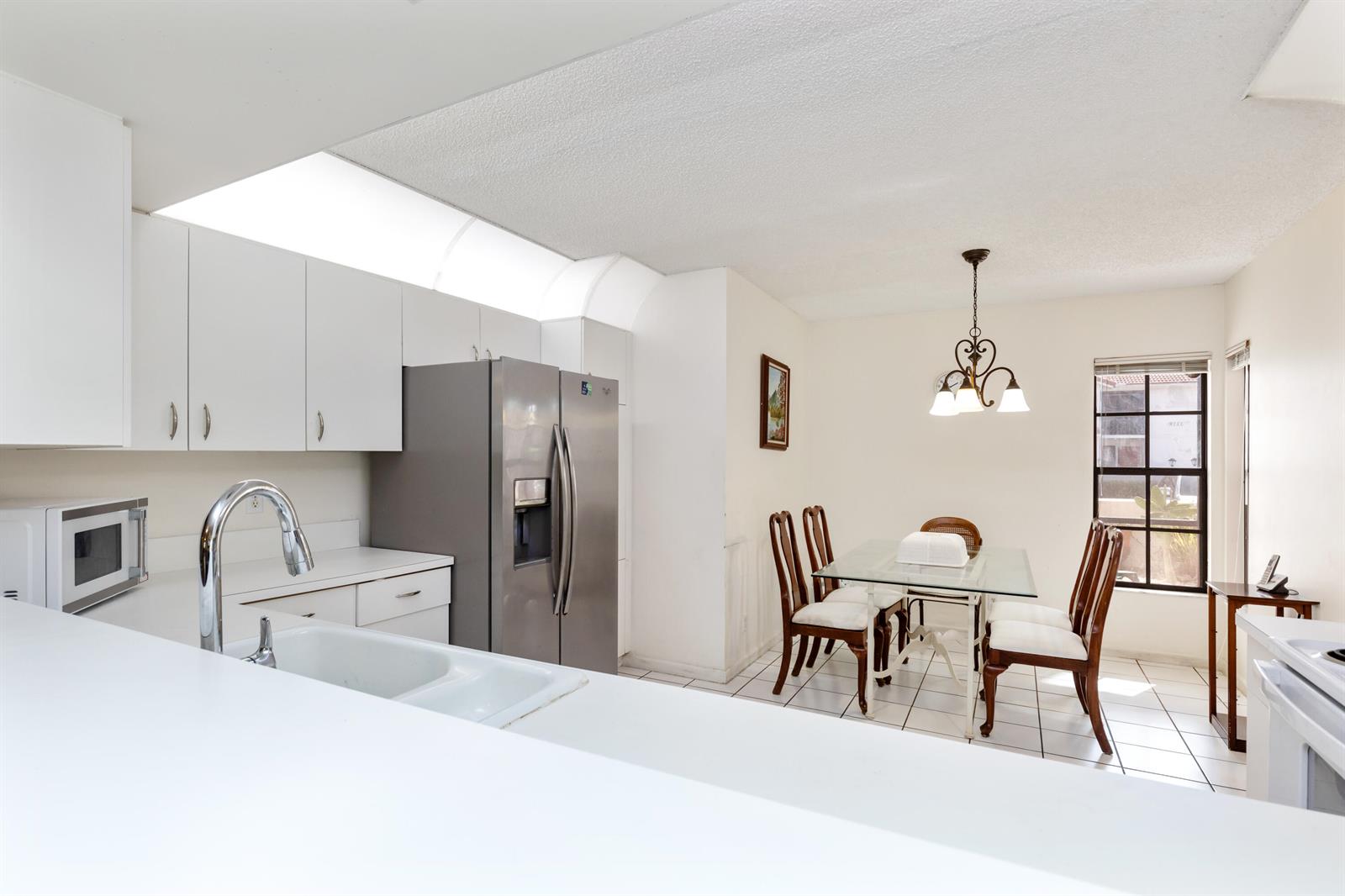 A kitchen with white cabinets and stainless steel appliances opens to a dining area — 9711 Pavarotti Terrace # 101, Boynton Beach FL 33437, BOYNTON BEACH, FL