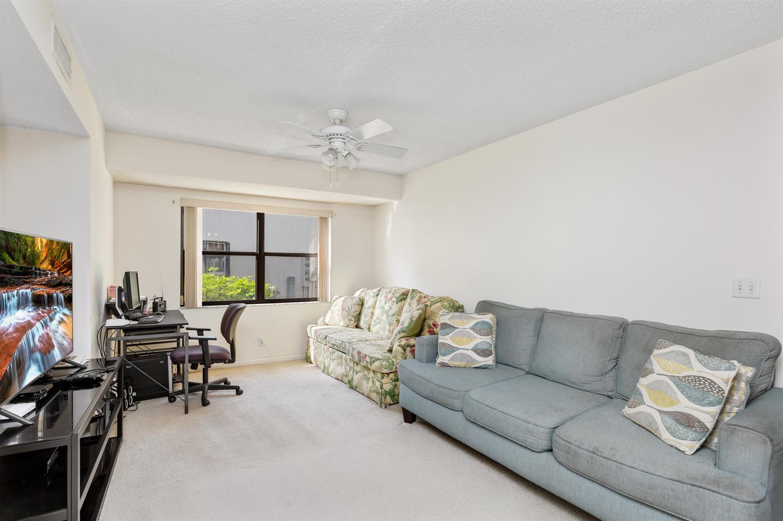 A living room features a blue sofa, a floral sofa, a desk, and a television — 9711 Pavarotti Terrace # 101, Boynton Beach FL 33437, BOYNTON BEACH, FL