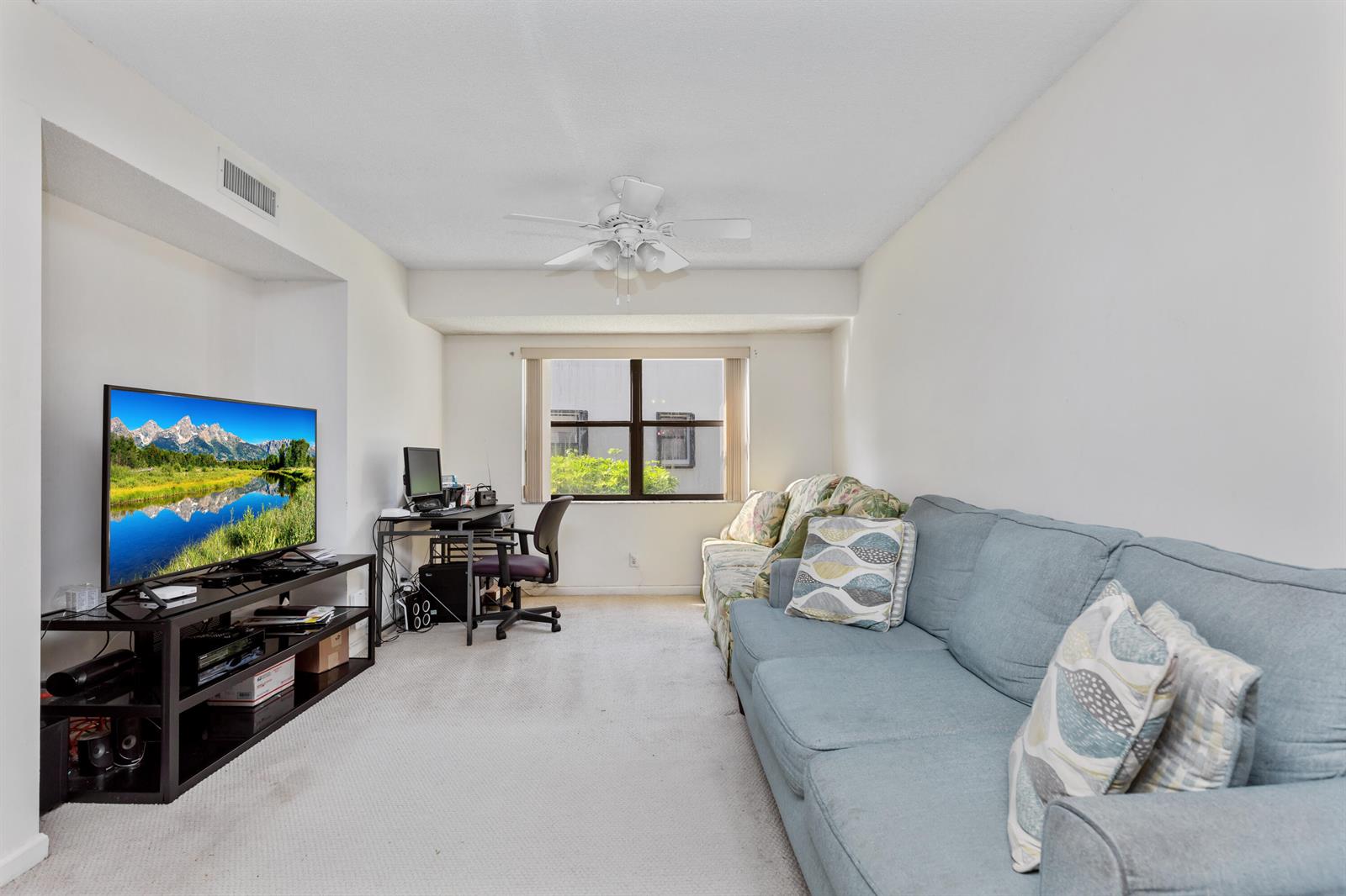 A living room features a blue sofa, a television on a stand, and a desk area — 9711 Pavarotti Terrace # 101, Boynton Beach FL 33437, BOYNTON BEACH, FL