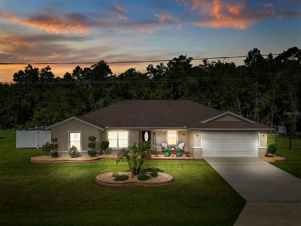 A single-story house with a tan exterior, brown roof, and concrete driveway at sunset — 15136 SE 93RD AVENUE, SUMMERFIELD, FL