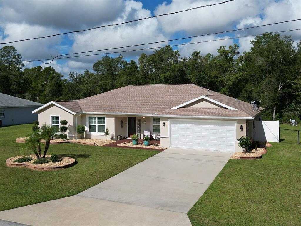 A single-story house with a beige exterior, a two-car garage, and a landscaped front yard — 15136 SE 93RD AVENUE, SUMMERFIELD, FL