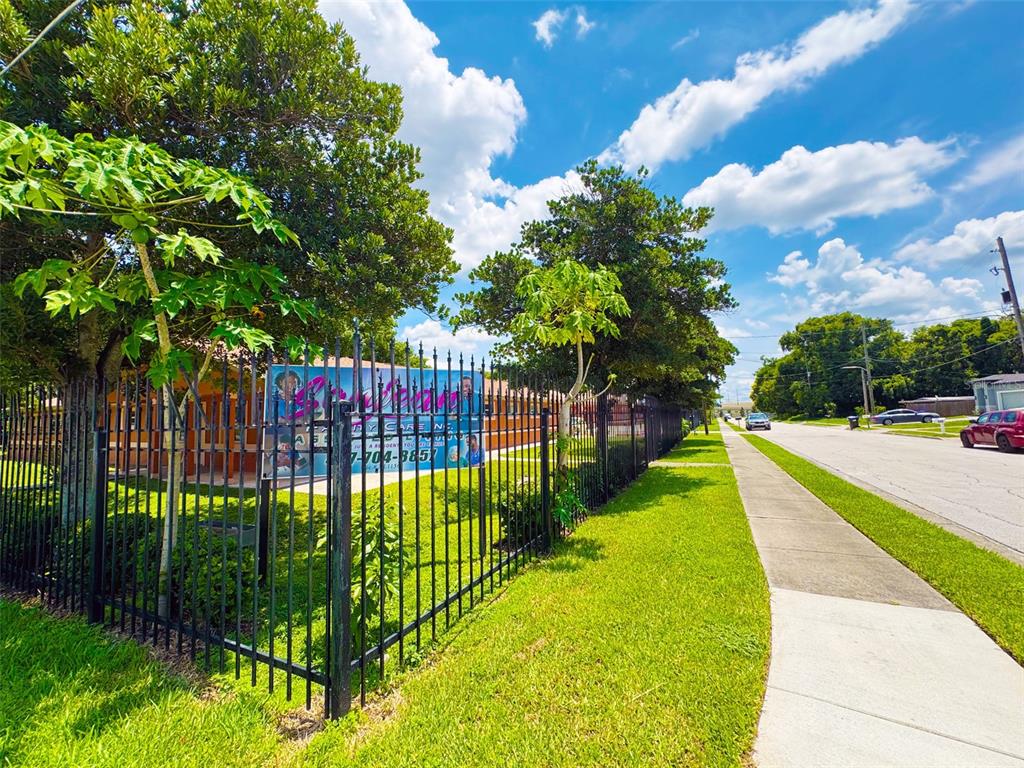 A black metal fence encloses a grassy yard with trees and a sign along a sidewalk — 815 24TH STREET, ORLANDO, FL