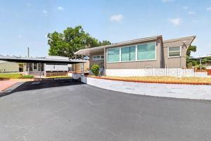 A single-story manufactured home features a carport, tan siding, and a low white retaining wall — 3896 PICCIOLA UNIT 224, FRUITLAND PARK, FL
