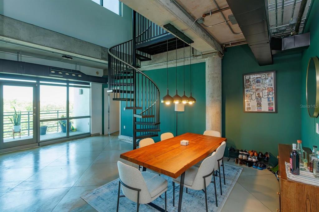 A dining area features a wooden table, spiral staircase, and teal walls in an industrial loft — 10 N SUMMERLIN AVENUE UNIT 55, ORLANDO, FL