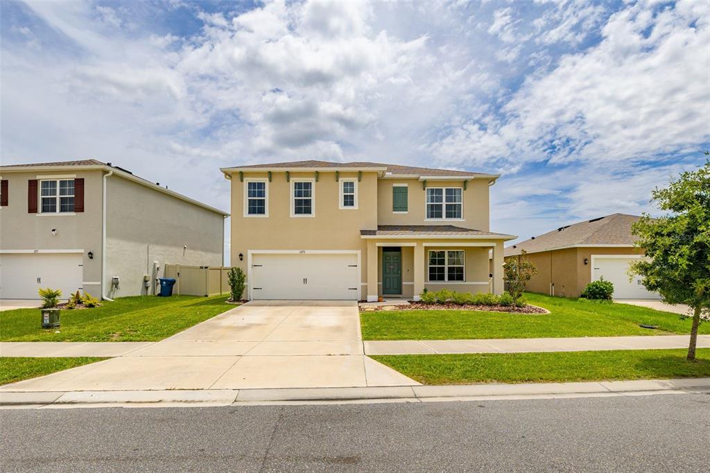 A two-story tan house with a two-car garage and a front porch under a cloudy sky — 1273 RED HILL ROAD, DAVENPORT, FL
