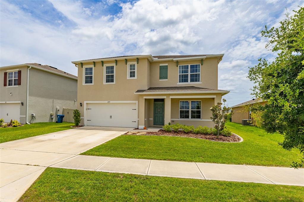 A two-story suburban house with a beige stucco exterior, a two-car garage, and a lawn — 1273 RED HILL ROAD, DAVENPORT, FL