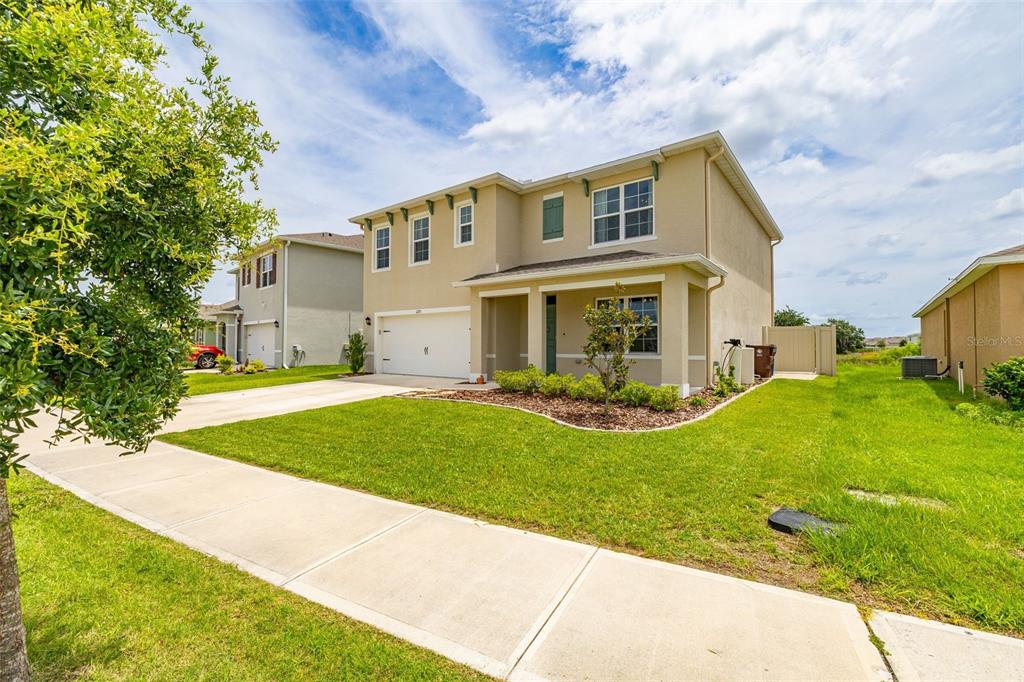 A two-story suburban house with a tan stucco exterior, a two-car garage, and a lawn — 1273 RED HILL ROAD, DAVENPORT, FL