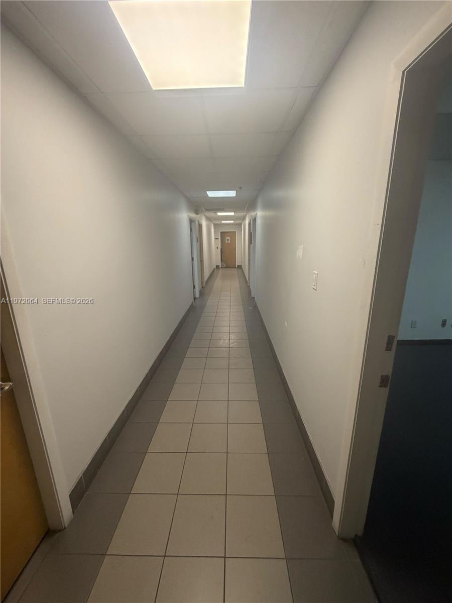 A long, narrow hallway features light-colored floor tiles and white walls with multiple doors — 13449 NW 42nd Ave, Opa-Locka FL 33054, OPA-LOCKA, FL